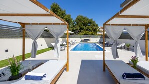 Ein Poolbereich mit zwei Holzliegen, einem Pool und einer Pergola.