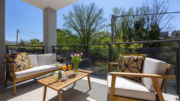 Ein Balkon mit einer Couch, Stühlen, einem Tisch und einer Blumenvase.
