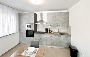 A modern kitchen with a built-in oven, microwave, and coffee maker, a dining area with a table set for two, and a trash bin. - Stunning home in Donji Prolozac (Donji Prolozac)