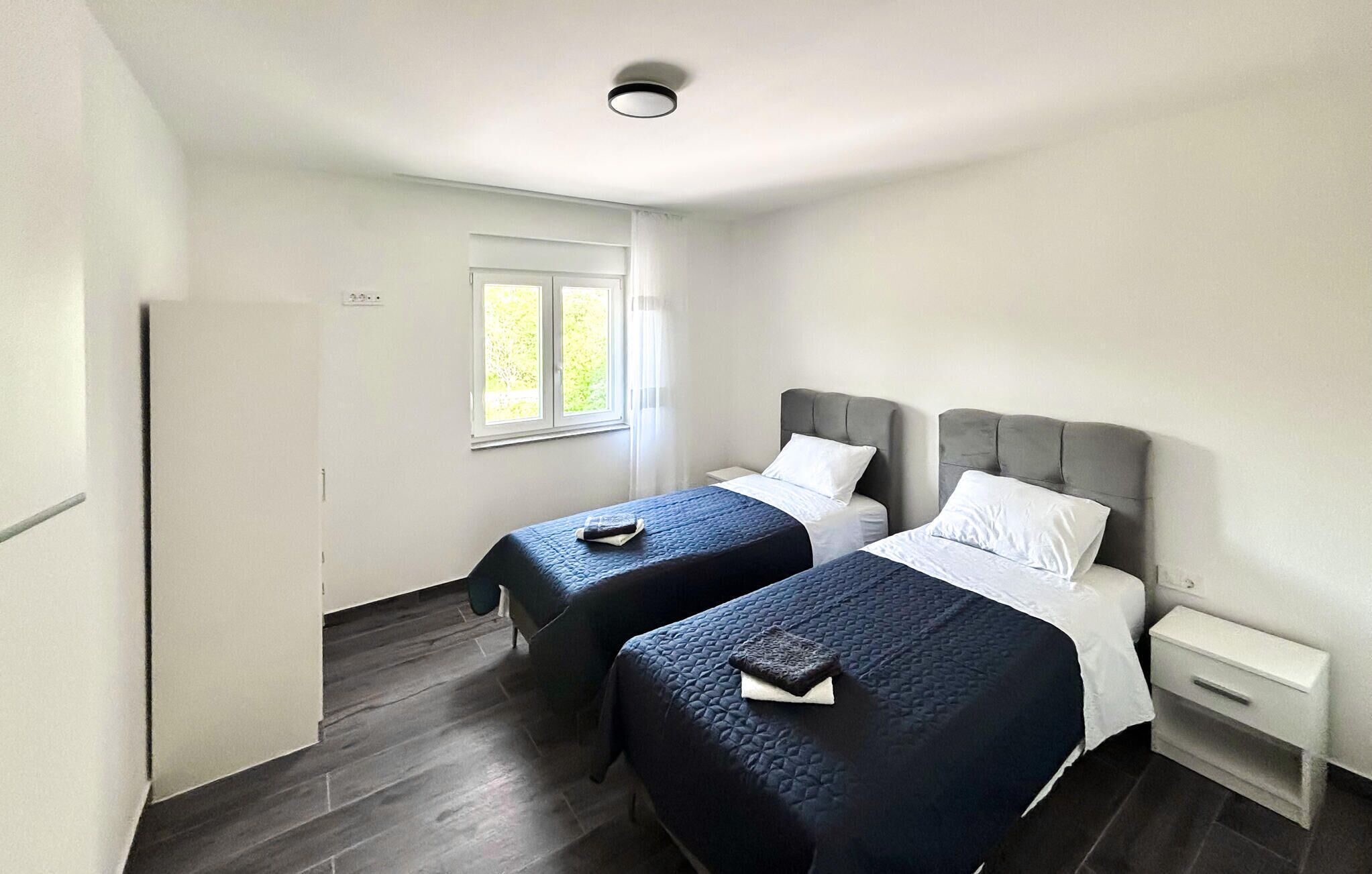 Quarto de hotel com duas camas, uma janela e uma pequena mesa de cabeceira.