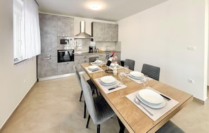 A modern kitchen with a dining area, featuring a wooden table set for four, a built-in oven, and a stainless steel range hood. - Stunning home in Donji Prolozac (Donji Prolozac)