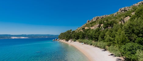 Una playa costera con aguas cristalinas, una orilla arenosa y una ladera boscosa.