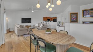 A modern living room with a dining area, wooden flooring, and a kitchen in the background. - Oceanside Vista - View of the Ocean from Balcony (Indialantic)