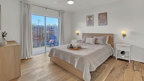 A bedroom with a bed, a nightstand, a ceiling fan, a window with curtains, and a view of the outside. - Oceanside Vista - View of the Ocean from Balcony (Indialantic)