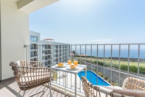 A balcony with wicker furniture, a table with croissants and orange juice, and a view of the sea and buildings. - Infinity Blue by Atlantic Holiday (Câmara de Lobos)