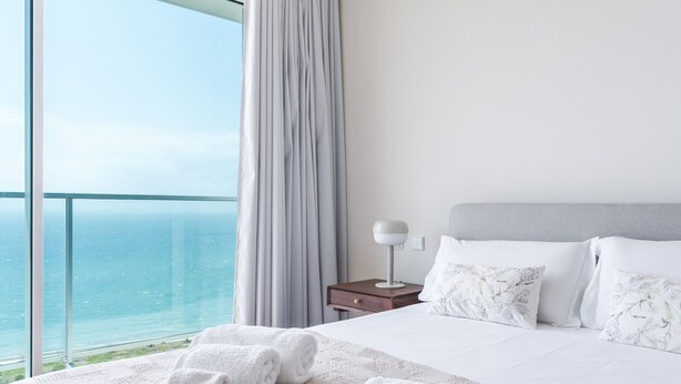 A hotel room with a large window, a bed with white linens, a nightstand with a lamp, and a view of the ocean. - La Belle Vie by Atlantic Holiday (Funchal)