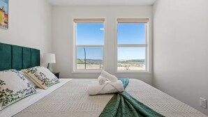 Una camera da letto con un letto, cuscini, una coperta, un comodino, una lampada e due finestre con vista sul paesaggio.