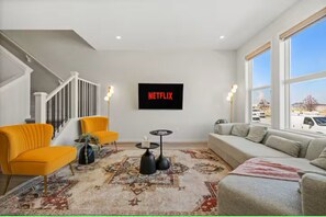 Ein Wohnzimmer mit Treppe, einer Couch, zwei Sesseln, einem Couchtisch und einem großen Fenster.