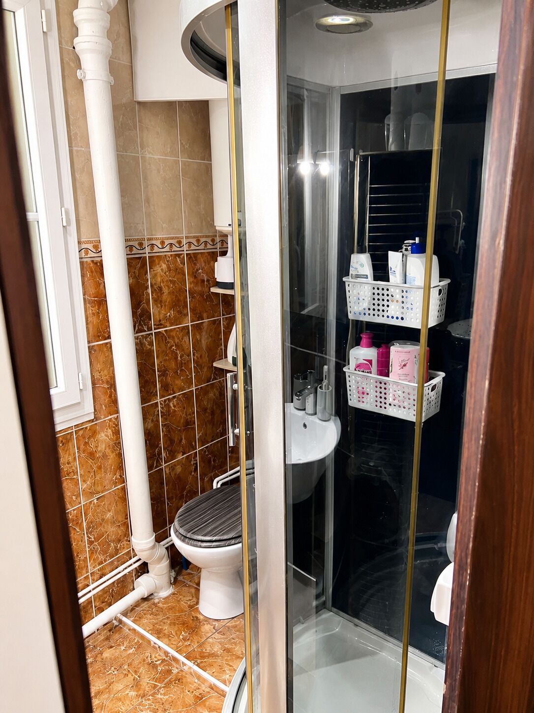 Une salle de bain avec des toilettes, un lavabo et une cabine de douche. Des paniers de rangement sont fixés au mur.
