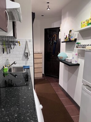 A modern kitchen with a black countertop, stainless steel sink, and a black refrigerator. - Charming and comfortable studio - Paris 14 (Paris)