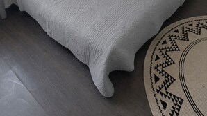 A single bed with a textured grey duvet and pillows, a round rug with a geometric pattern, and a white wall. - Charming and comfortable studio - Paris 14 (Paris)