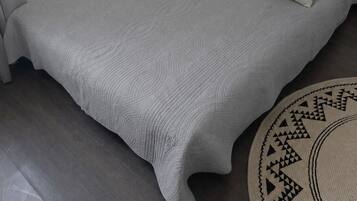 Ein Einzelbett mit einer strukturierten, grauen Bettdecke und Kissen, ein runder Teppich mit geometrischem Muster und eine weiße Wand.