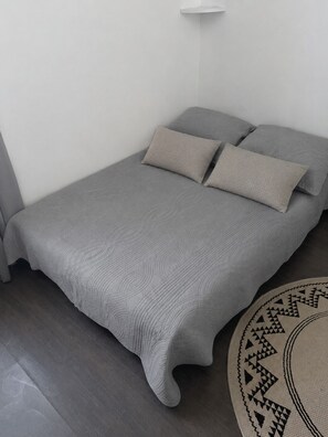 A single bed with a textured grey duvet and pillows, a round rug with a geometric pattern, and a white wall. - Charming and comfortable studio - Paris 14 (Paris)