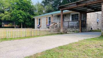 A building with a covered porch, a gravel driveway, and a wooden fence.