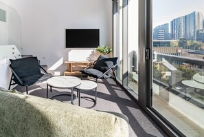 Ein moderner Balkon mit einer Couch, zwei Stühlen, einem kleinen Tisch und einem Fernseher.