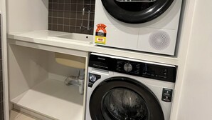 Un cuarto de lavandería con dos lavadoras de carga frontal, un estante arriba y un salpicadero de azulejos.