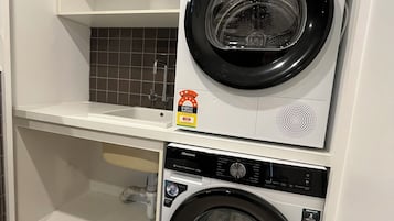 A laundry room with two front-loading washing machines, a shelf above, and a tiled backsplash.