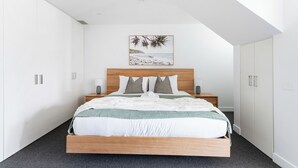 Un dormitorio con cama, mesitas de noche, lámpara de techo, una obra de arte en la pared y armarios blancos.