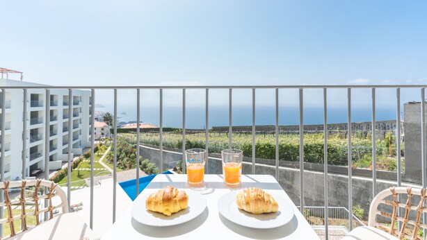 A balcony with two croissants and two glasses of orange juice, overlooking a vineyard and a coastal view. - Infinity Blue by Atlantic Holiday (Camara de Lobos)