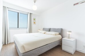 Ein Schlafzimmer mit einem Bett, Nachttischen, einer Fenster und einer an der Wand befestigten Leuchte.