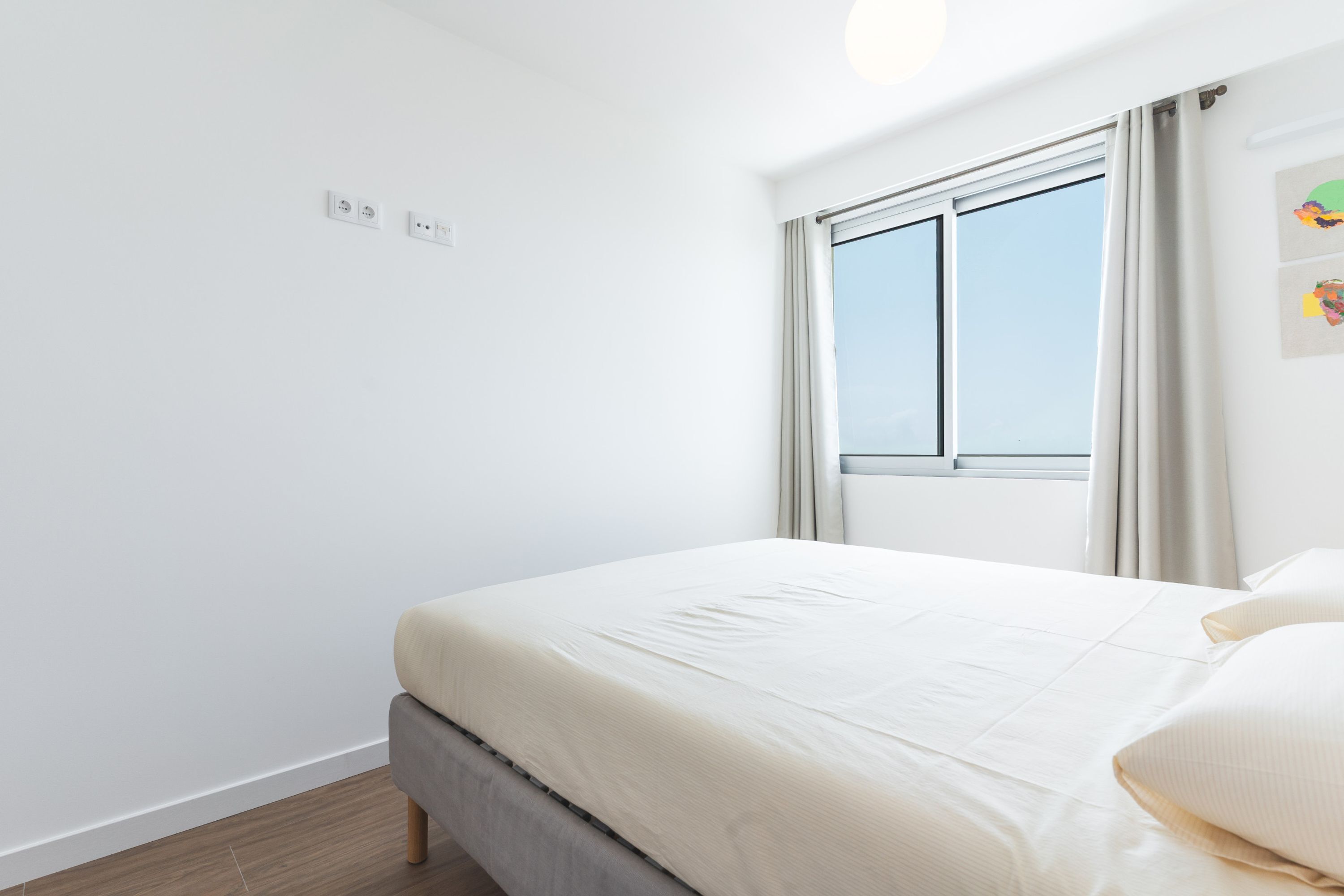 A minimalist bedroom with a bed, a window, and a wall-mounted light fixture.
