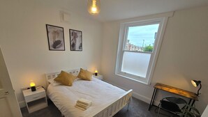 Ein Schlafzimmer mit einem Bett, zwei Nachttischlampen, einem Fenster und einem Schreibtisch mit Lampe.