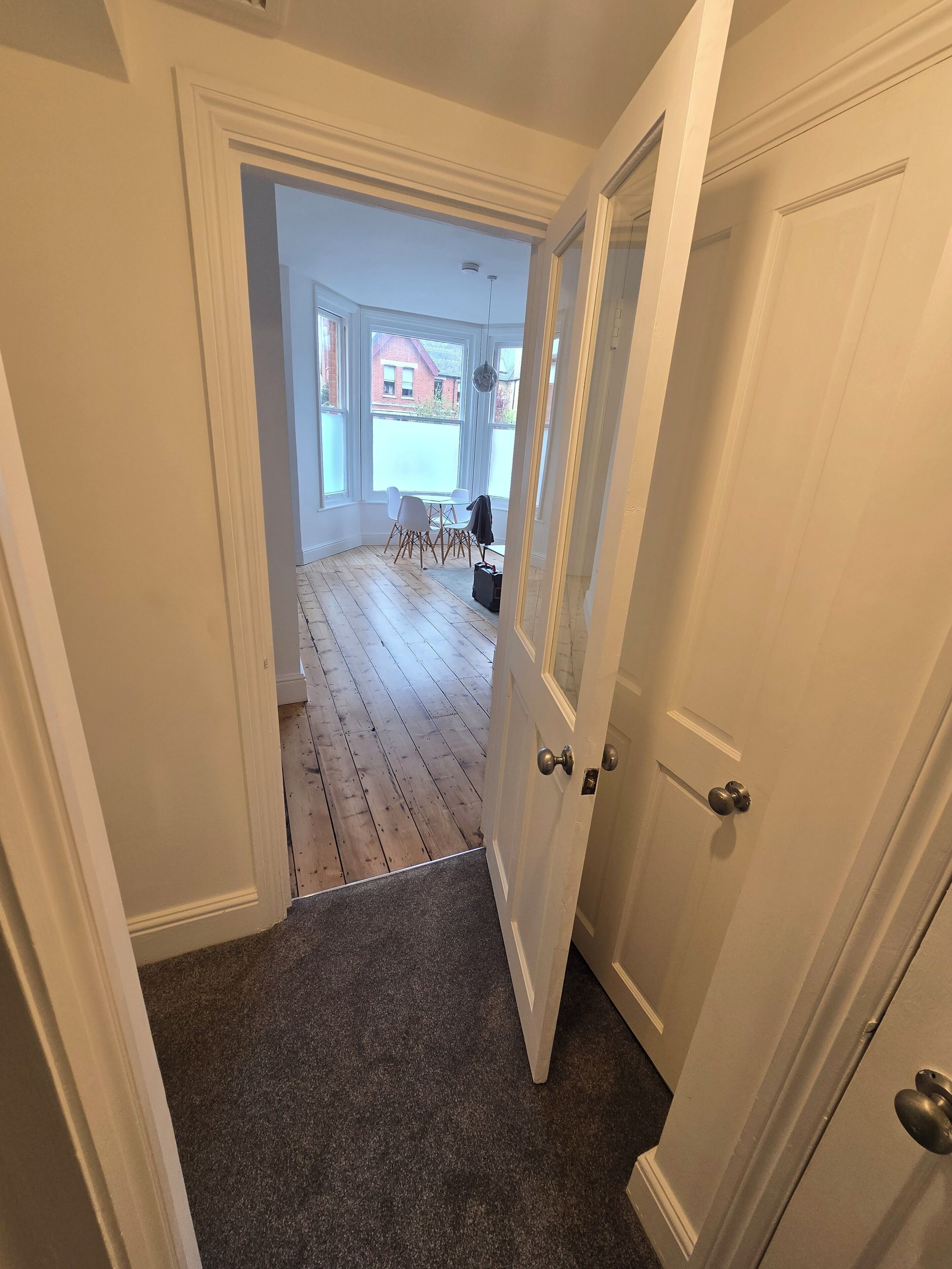 A hallway leading to a room with a view of a red brick building outside.