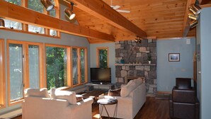 Ein geräumiges Wohnzimmer mit großen Fenstern, einem Kamin aus Stein und einem Fernseher.