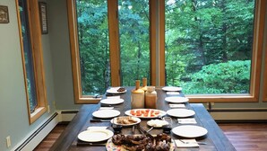 Ein Esszimmer mit gedecktem Tisch und Blick auf einen Wald durch große Fenster.