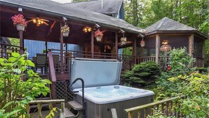Ein Whirlpool auf einer Holzterrasse mit Überdachung und hängenden Blumentöpfen.