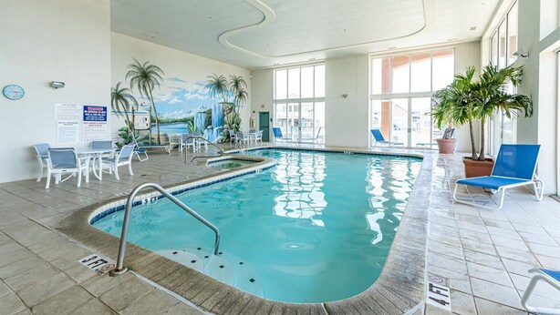 An indoor swimming pool with clear water, surrounded by lounge chairs and potted plants. - Three Bedroom Oceanside Condo with Great Amenities (Ocean City)