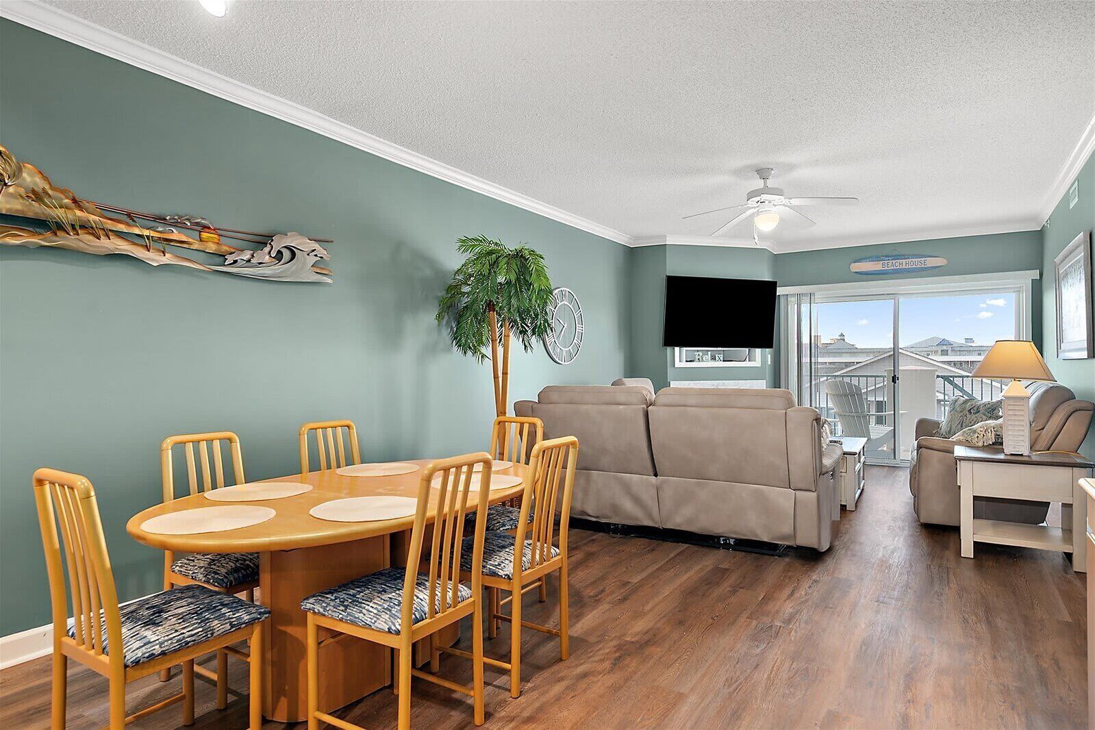 A living room with a dining area, a sofa, a TV, and a balcony with a view.
