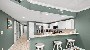 A modern kitchen with white cabinets, a stainless steel refrigerator, and a bar area with stools. - Three Bedroom Oceanside Condo with Great Amenities (Ocean City)