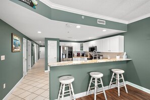 A modern kitchen with white cabinets, a stainless steel refrigerator, and a bar area with stools. - Three Bedroom Oceanside Condo with Great Amenities (Ocean City)