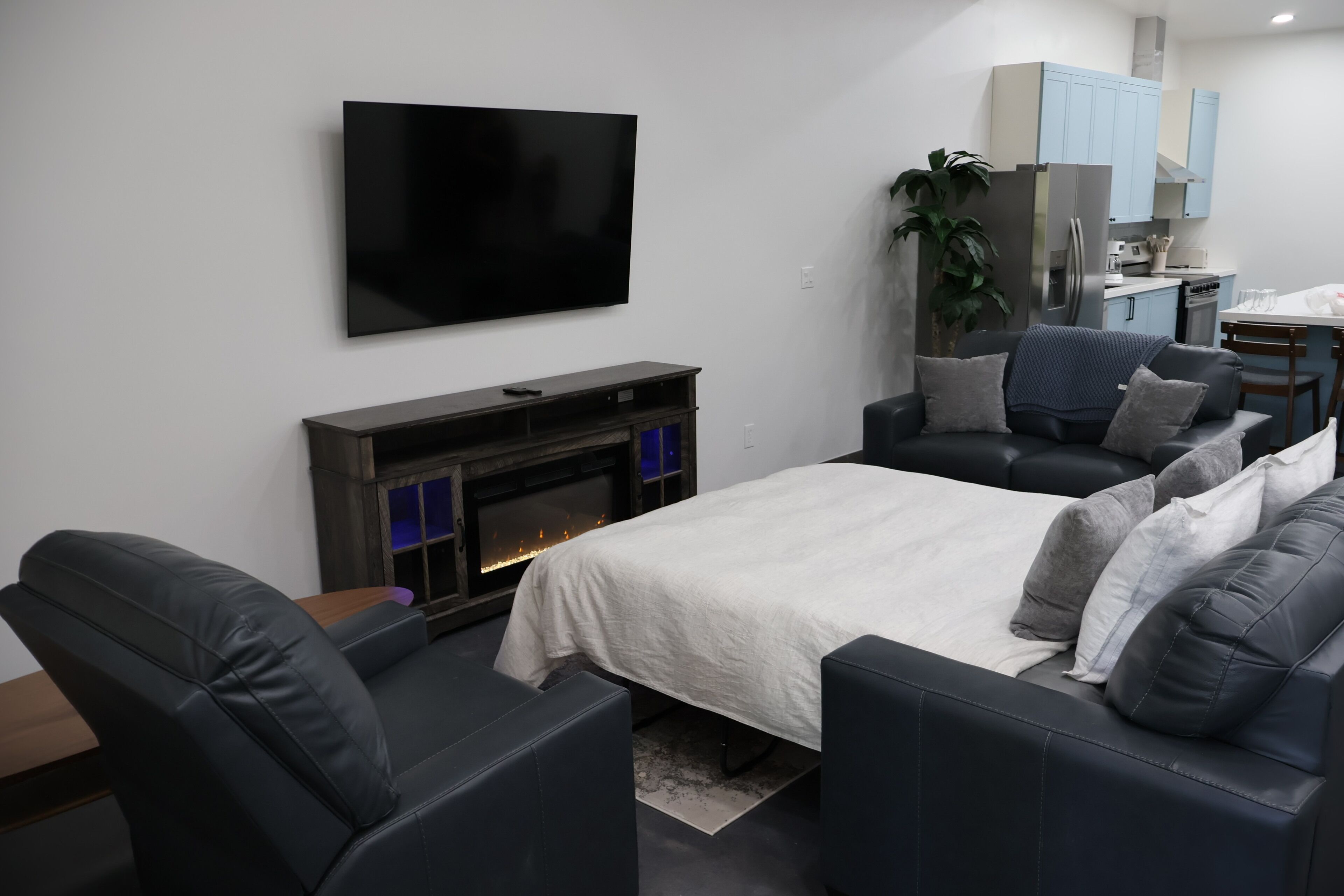 A modern living room with a flat-screen TV, a fireplace, a sofa, and a dining area with light blue cabinets.