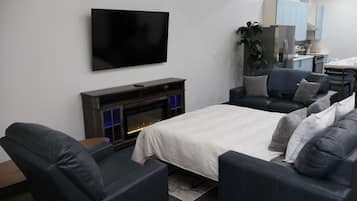 A modern living room with a flat-screen TV, a fireplace, a sofa, and a dining area with light blue cabinets.