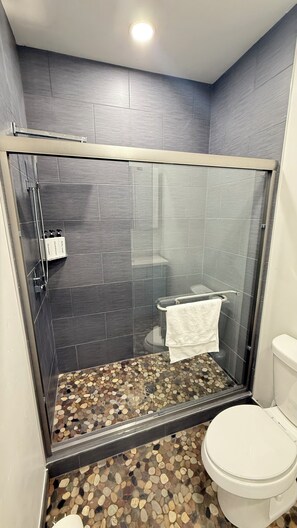 Une douche avec une porte en verre, un sol carrelé et des toilettes.