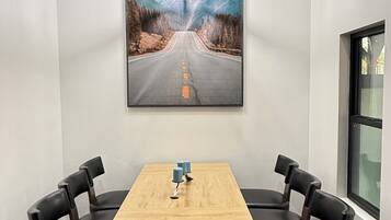 A conference room with a wooden table, four chairs, a painting of a road, and a hanging light fixture.