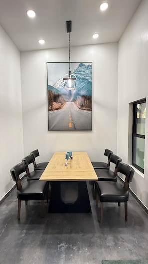 Une salle de conférence avec une table en bois, quatre chaises, un tableau représentant une route et un luminaire suspendu.