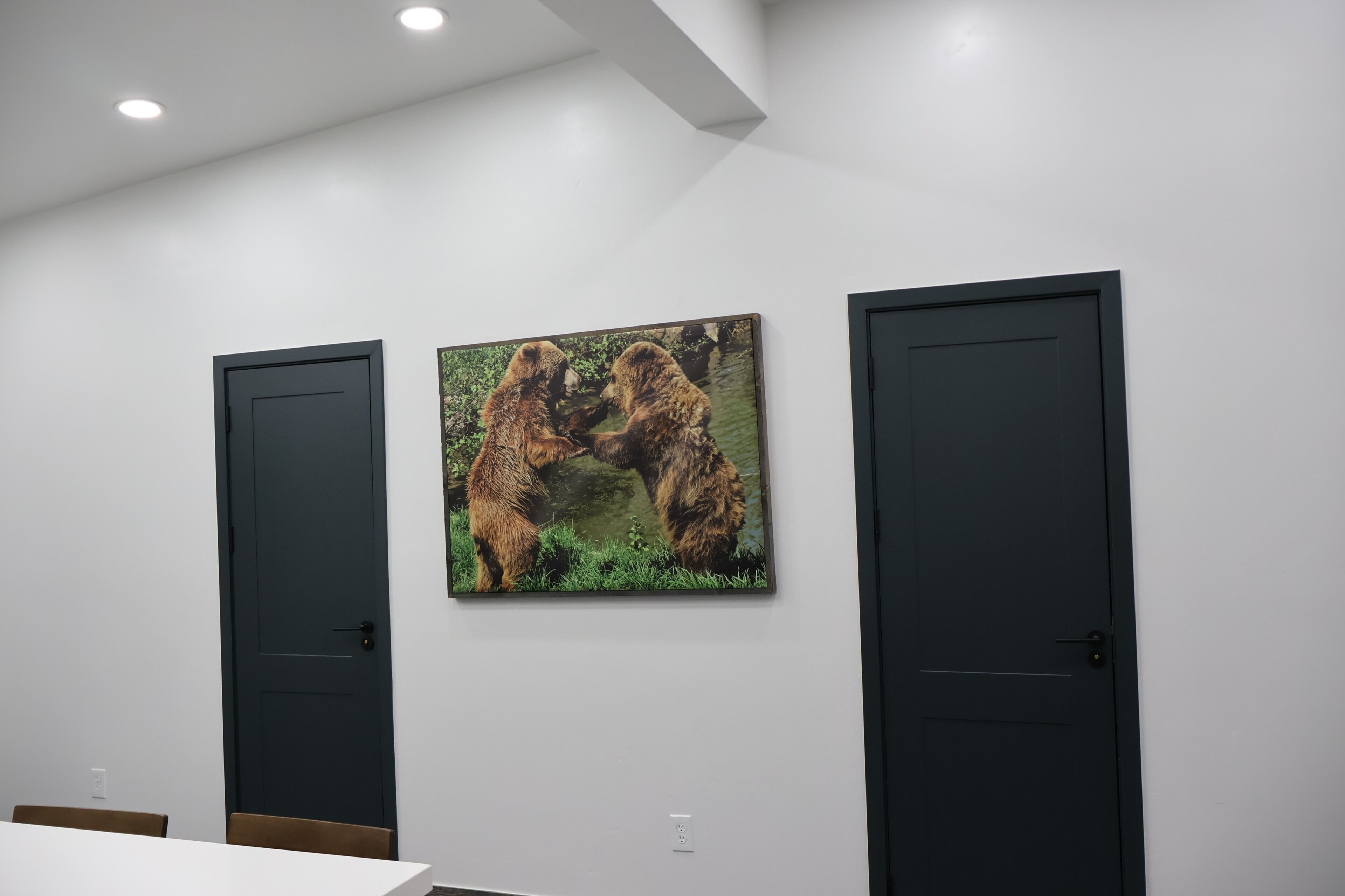 A room with a white wall, two black doors, and a framed picture of bears.
