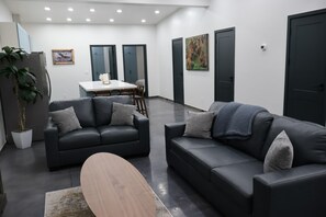 A modern living room with two black leather sofas, a wooden coffee table, a dining table with chairs, and a potted plant. - Glacier Luxury Retreat / Montana Sky Apartment 2 (Hungry Horse)