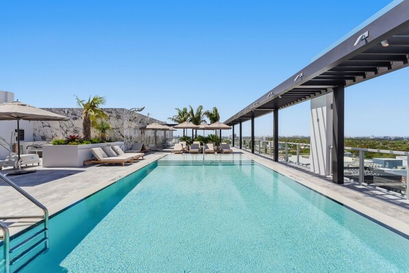 Ein Pool auf dem Dach mit Liegestühlen, Sonnenschirmen und freier Aussicht auf die Stadt.