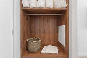 Ein Holzschrank mit Regalen, einem Korbwäsche und einer weißen Decke.