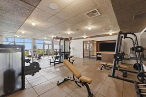 Ein Fitnessraum mit Trainingsgeräten, einer Bank und Blick ins Freie.