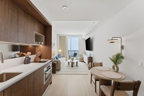 Eine moderne Küche mit Holzausstattung, ein Essbereich mit rundem Tisch und Stühlen, ein Wohnzimmer mit Sofa und Fernseher sowie Meerblick.