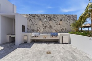 Eine Außenküche mit Marmor-Spritzschutz, einem eingebauten Grill und einem kleinen Kühlschrank.