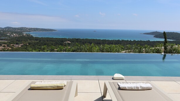 An infinity pool with a view of the sea and hills, two lounge chairs with towels, and a water feature. - Villa Sarra Di Pinarellu (Zonza)