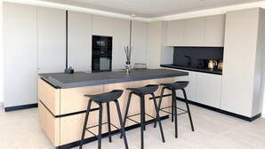 A modern kitchen with a central island, bar stools, and built-in appliances. - Villa Sarra Di Pinarellu (Zonza)