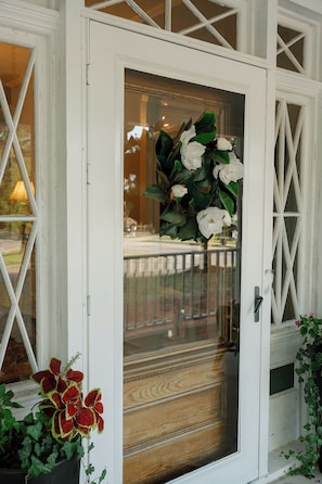 Una puerta blanca con un panel de vidrio, una reja de metal y una planta en maceta con hojas rojas y verdes.