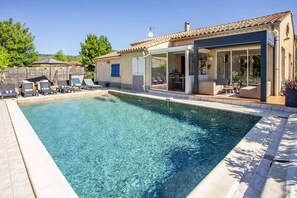 A swimming pool with clear water, surrounded by lounge chairs and a covered outdoor seating area. - Villa Repose by Villa Plus (Argeliers)
